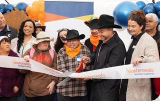 A candid group photo of leadership, participants, and associates cutting a ribbon for a grand opening.