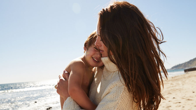 Claire holding toddler in diaper on beach